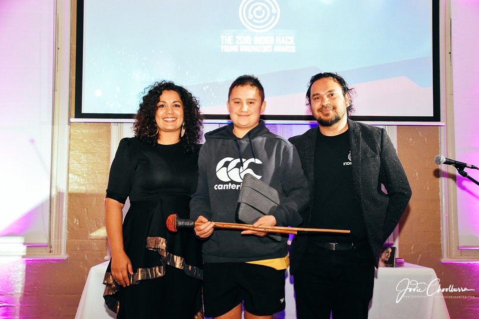 15 year old Te Ākauroa Jacob holds a jimal - firestick with Deline and Luke Briscoe in front of Indigihack logo