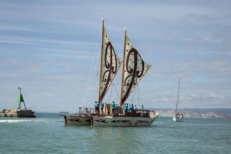 Image shows a double hulled waka with beautiful Māori designs on the water